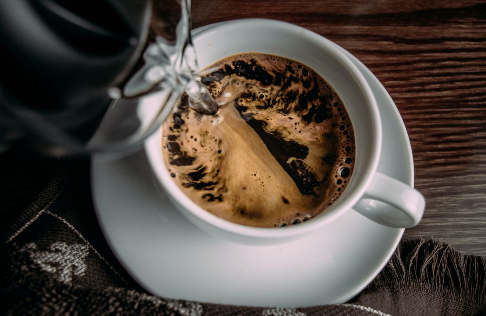 Un jarra vierte agua sobre una taza con café liofilizado